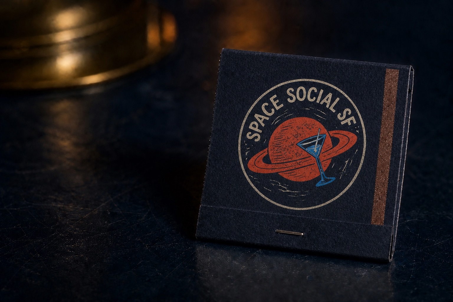 Concept mockup of a matte navy Space Social SF matchbook on a dark bar top